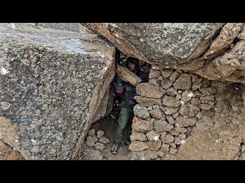 Building a secret warm stone shelter under a large rock,snowy winter survival camping